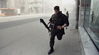 Bosnian army member sprints for cover after a tank round, fired by Yugoslav People's Army, struck an apartment house across the street in Sarajevo on 2 May 1992