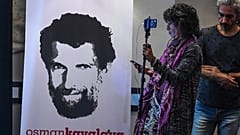 A journalist stands in front of a poster featuring jailed businessman and philanthropist Osman Kavala.