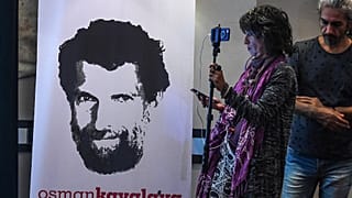 A journalist stands in front of a poster featuring jailed businessman and philanthropist Osman Kavala.
