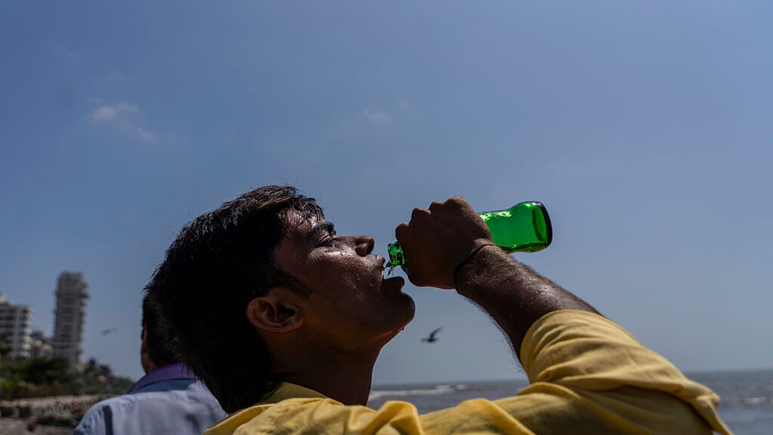 Un homme boit un soda au cours d'une promenade sur les côtes de la mer d'Arabie à Mumbai, Inde (1er mai 2022).