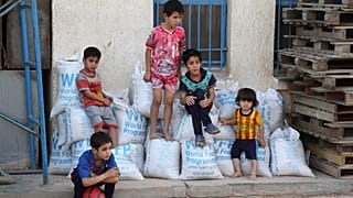 Children sit on bags of rice from the World Food Program (WFP) at a school that serves as a shelter for internally displaced people in Baghdad's eastern district of Jamila.