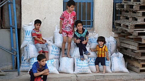 Children sit on bags of rice from the World Food Program (WFP) at a school that serves as a shelter for internally displaced people in Baghdad's eastern district of Jamila.