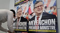 A supporter of far-left leader Jean-Luc Melenchon sticks electoral posters reading "Melenchon Prime Minister" before a local meeting, Thursday, May 5, 2022 in Lille.