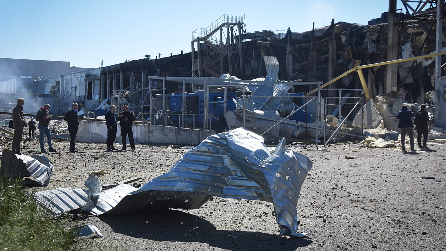 People stand near a destroyed building on the outskirts of Odesa, Ukraine, Tuesday, May 10, 2022. A shopping centre and a warehouse were destroyed in the Russian strike.