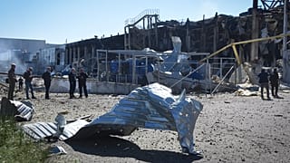 People stand near a destroyed building on the outskirts of Odesa, Ukraine, Tuesday, May 10, 2022. A shopping centre and a warehouse were destroyed in the Russian strike.