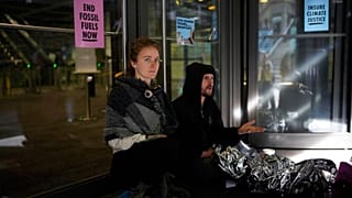 An Extinction Rebellion climate change protester sits with a lock around her neck attached to a bar on a door.