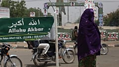 سيدة مسلمة تمر بجانب لافتة كتب عليها "الله أكبر" في كاتسينا، نيجيريا.
