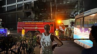 A person watches as fire officials douse a fire in a four storied building, in New Delhi, India, Saturday, May 14, 2022.