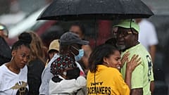 Bystanders gather under an umbrella as rain rolls in after a shooting at a supermarket on Saturday, May 14, 2022, in Buffalo, N.Y.