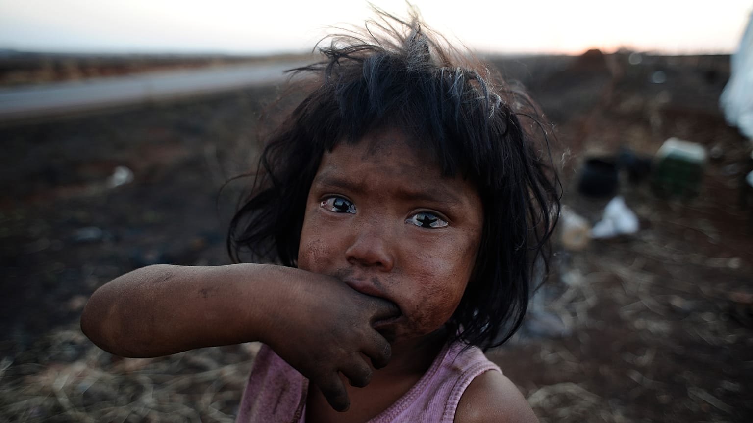 Guarani Kaiowa Indian girl cries in front of her hut destroyed by a fire set by an unknown arsonist in their makeshift camp close to their ancestral land.