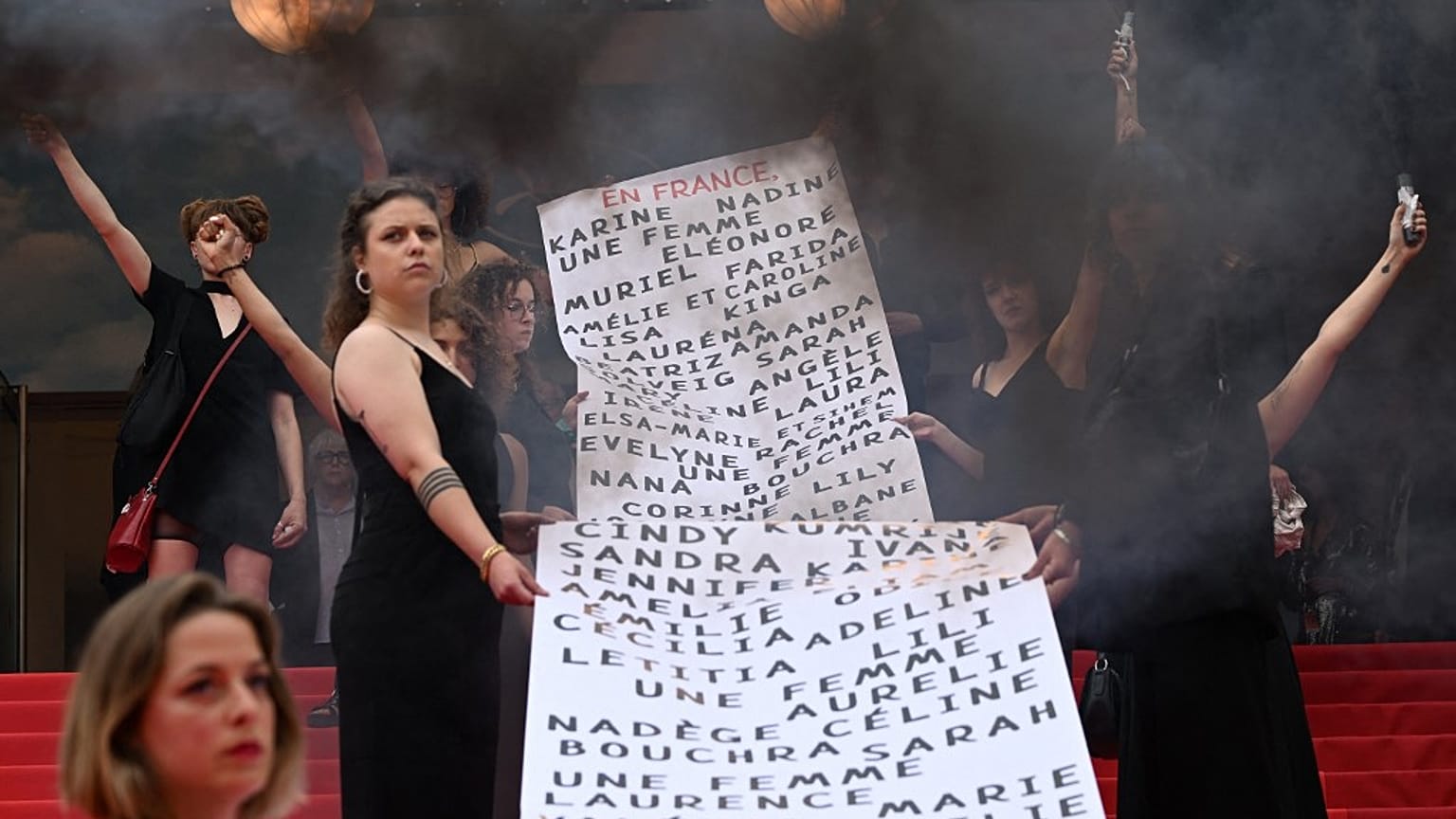 "Les Colleuses" hold a banner with names of 129 women who died in the last 12 months