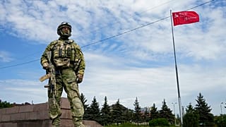 Orosz katona Herszonban, háttérben egy szovjet győzelmi zászlóval