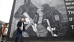 L'attivista lealista Jamie Bryson cammina davanti a un murale dell'Ulster Volunteer Force nella zona est di Belfast, Irlanda del Nord, 15 ottobre 2019. 