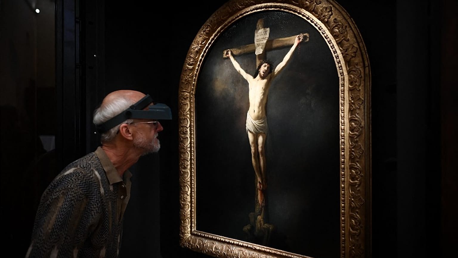 A French painting restorer inspects a 1631 oil on canvas painting by Rembrandt, "The Christ on the Cross" 