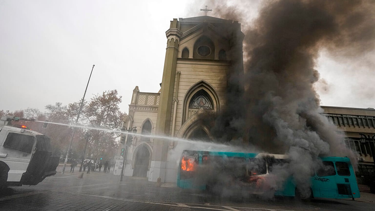 A police water cannon extinguishes a burning bus.
