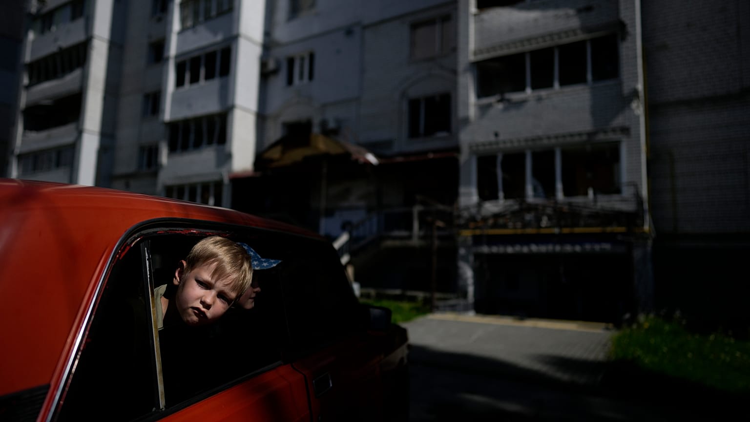 Kinder in einem Auto vor einem durch Angriffe zerstörten Gebäude in Borodjanka, am Stadtrand von Kiew (31. Mai 2022)