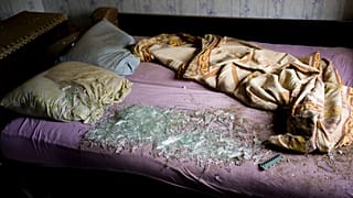 Осколки стекла на кровати в доме, пострадавшем после артобстрела Дружковки