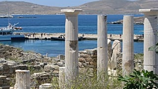 Antiguas estatuas y columnas de una casa milenaria encima del muelle de desembarco en el parque arqueológico de Delos, Grecia, el 25 de mayo de 2019