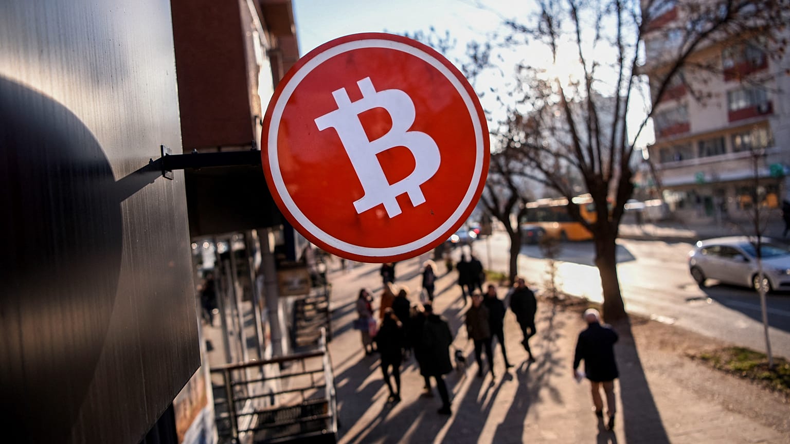 Bitcoin symbol above a shop as people walk by.