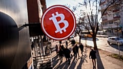 Bitcoin symbol above a shop as people walk by.