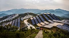 People walk past solar panels at a photovoltaic power station in Songxi county in southeastern China's Fujian province. 