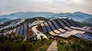 People walk past solar panels at a photovoltaic power station in Songxi county in southeastern China's Fujian province. 