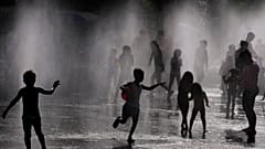 Children and adults cool off in a fountain in a park by the river in Madrid, Spain, Sunday, June 12, 2022.
