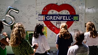 People observe the memorial, near to the remains of the Grenfell Tower.