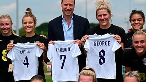 Prince William holding the England football jersey bearing the names of his three children and with the England women football team