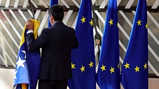 A member of protocol sets out EU and Bosnian flags prior to arrivals for an EU summit in Brussels, 23 June 2022