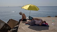 Una mujer duerme bajo una sombrilla en un rompeolas frente al mar Mediterráneo en Barcelona, España, el jueves 16 de junio de 2022.