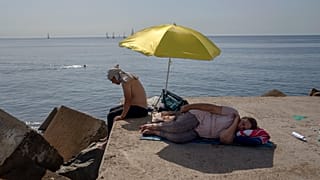 Una mujer duerme bajo una sombrilla en un rompeolas frente al mar Mediterráneo en Barcelona, España, el jueves 16 de junio de 2022.