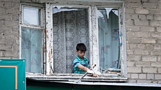 Мальчик убирает осколки разбитого оконного стекла после обстрела города Бахмут в Донецкой области