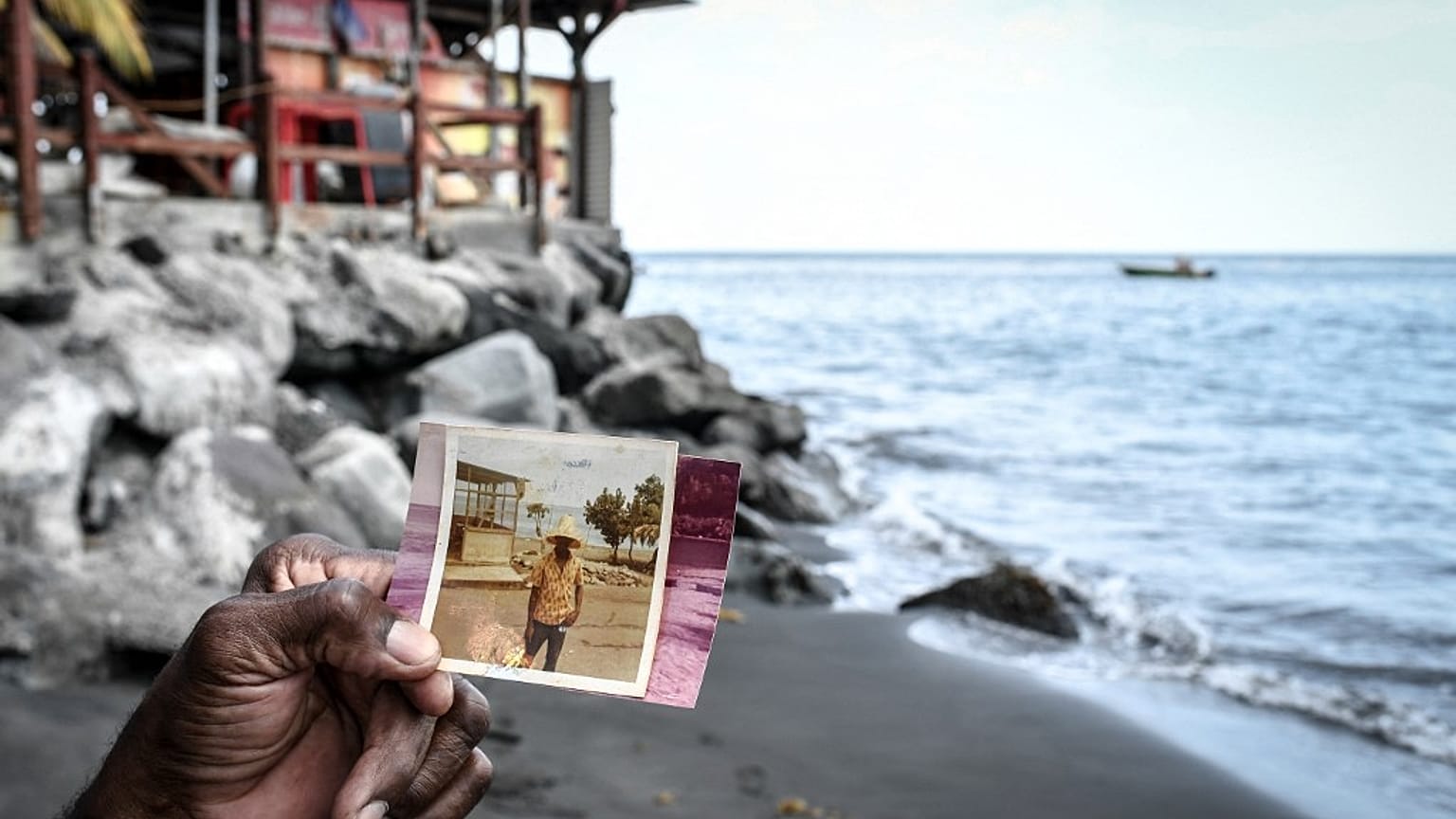 Joseph Gustave, propriétaire du restaurant Mélodie, compare la même plage à 50 ans d’écart, sur la plage du Prêcheur, en Martinique, le 17 juin 2022. 