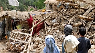 Afghan children stand near a house that was destroyed in an earthquake