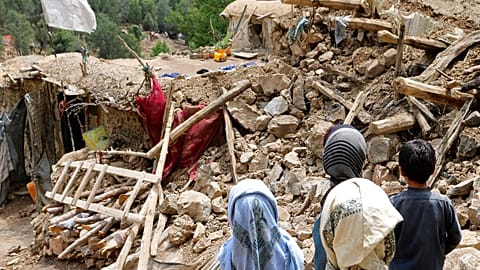 Afghan children stand near a house that was destroyed in an earthquake