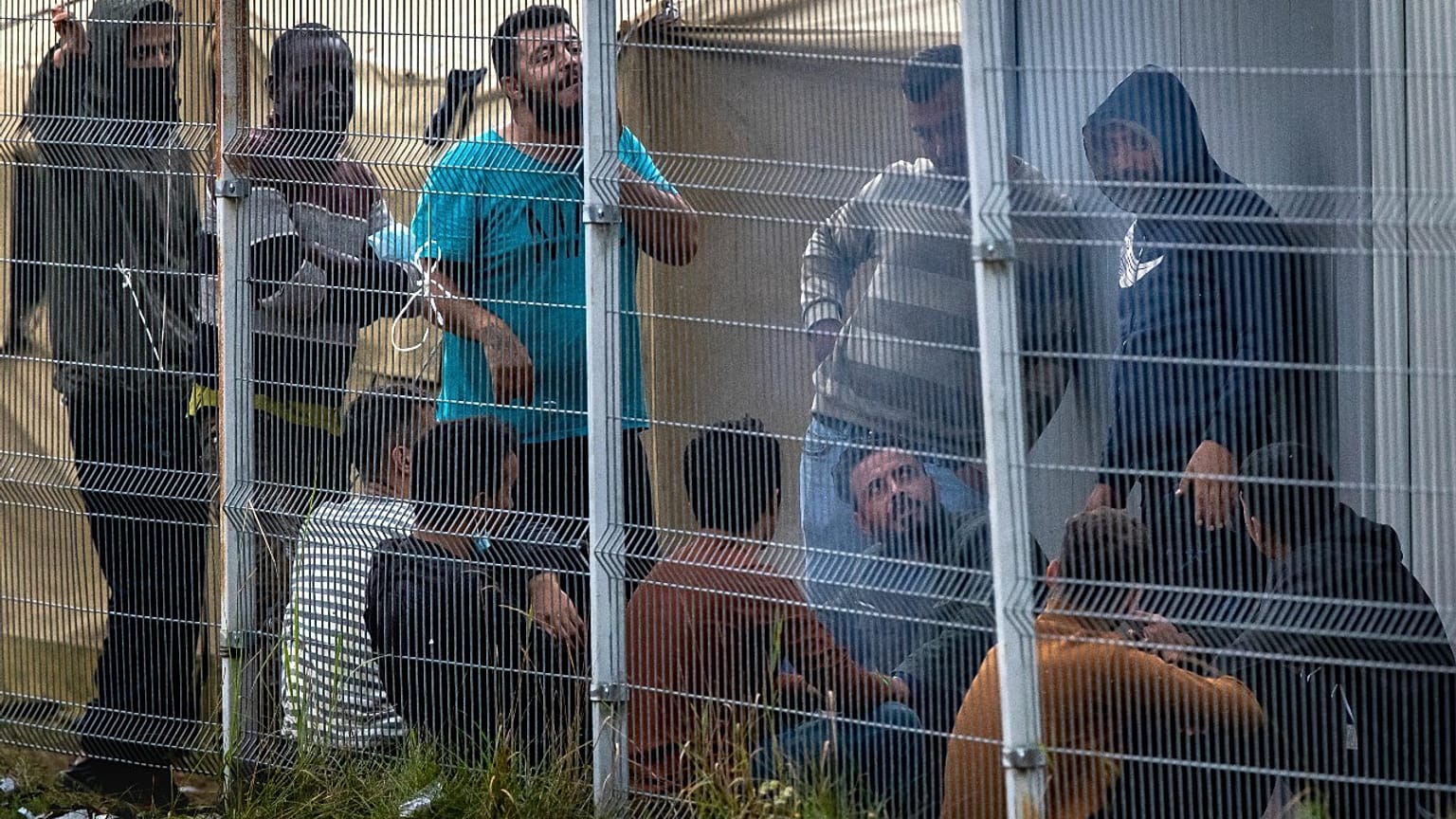 Migrants rest behind a fence inside the refugee camp in the Rudninkai military training ground, 38km south from Vilnius, Lithuania, Wednesday, Aug. 11, 2021.  