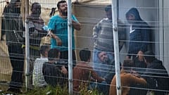 Migrants rest behind a fence inside the refugee camp in the Rudninkai military training ground, 38km south from Vilnius, Lithuania, Wednesday, Aug. 11, 2021.  