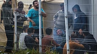 Migrants rest behind a fence inside the refugee camp in the Rudninkai military training ground, 38km south from Vilnius, Lithuania, Wednesday, Aug. 11, 2021.  