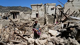 Un homme tenant un bébé au milieu de maisons en ruines dans la proivince de Paktika (26/06/2022)
