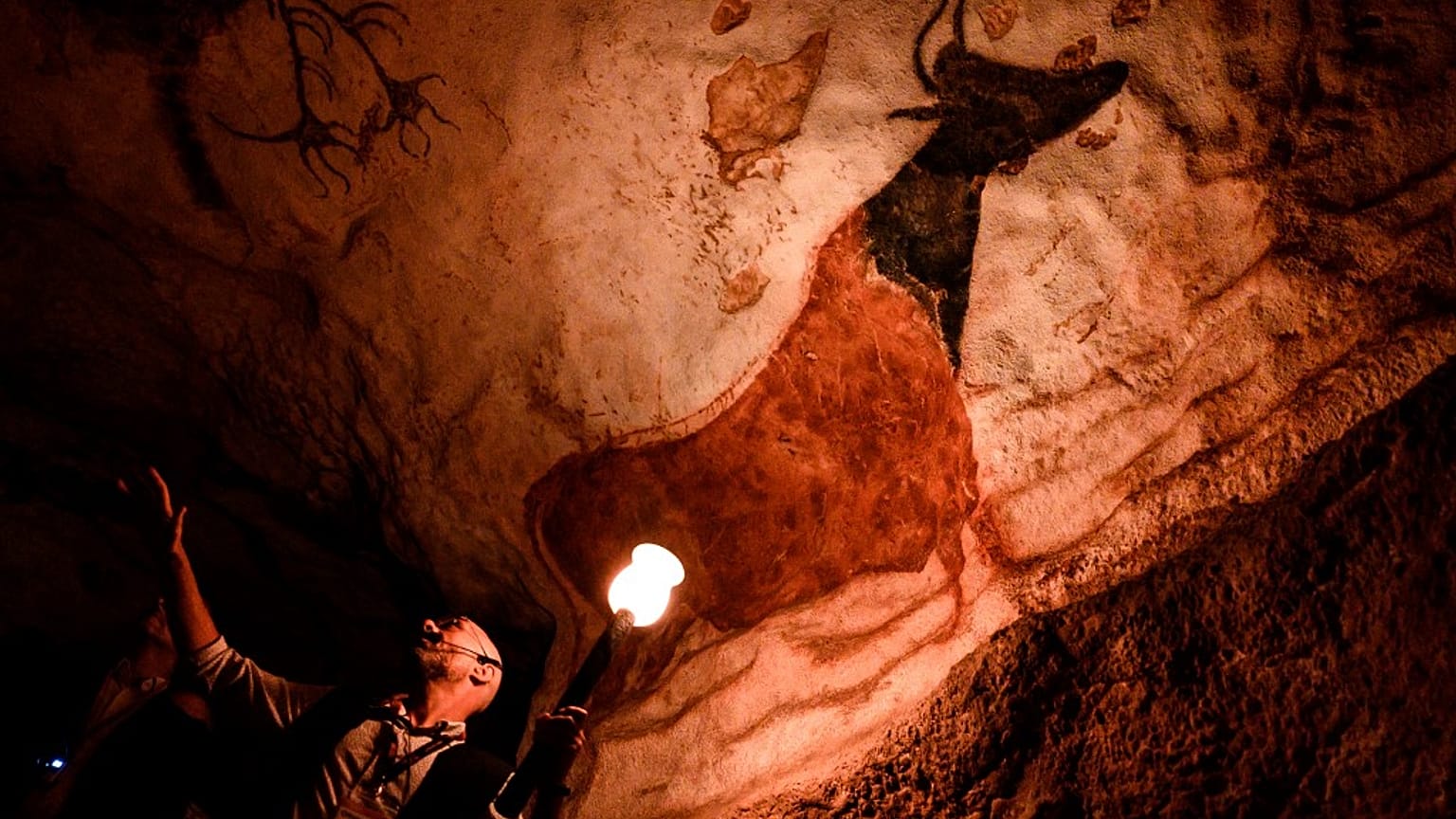 An employee shows paintings inside the life size Lascaux cave replica during a special immersive torch light visit on June 16, 2022 in Montignac.