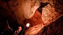 An employee shows paintings inside the life size Lascaux cave replica during a special immersive torch light visit on June 16, 2022 in Montignac.