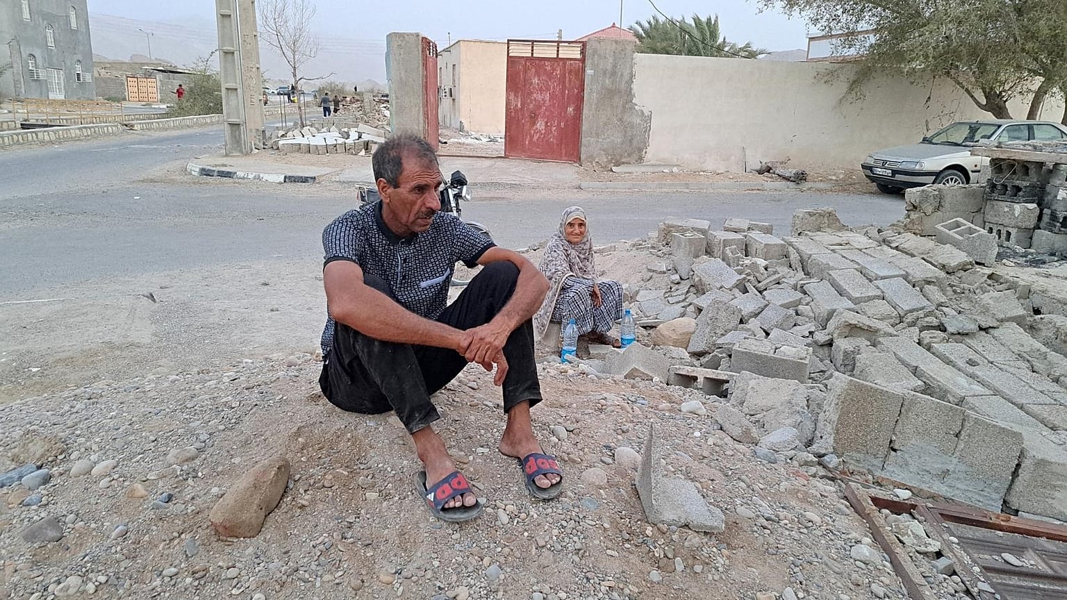 People sit by the rubble amidst destruction in the aftermath of a 6.0 magnitude earthquake in Iran's southern Hormozgan province on 2 July. 2022