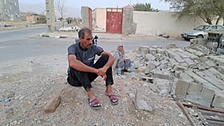 People sit by the rubble amidst destruction in the aftermath of a 6.0 magnitude earthquake in Iran's southern Hormozgan province on 2 July. 2022