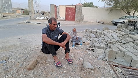 People sit by the rubble amidst destruction in the aftermath of a 6.0 magnitude earthquake in Iran's southern Hormozgan province on 2 July. 2022