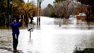 A man takes pictures of the flooded streets due to torrential rain in the Camden suburb of Sydney on July 3, 2022.