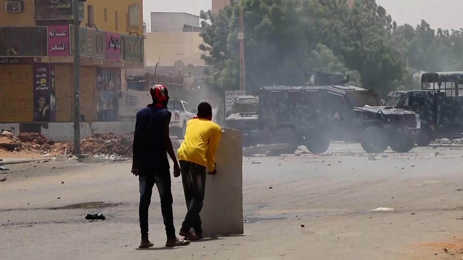 Protesters carrying shields and throwing stones towards armoured vehicle, security firing tear gas