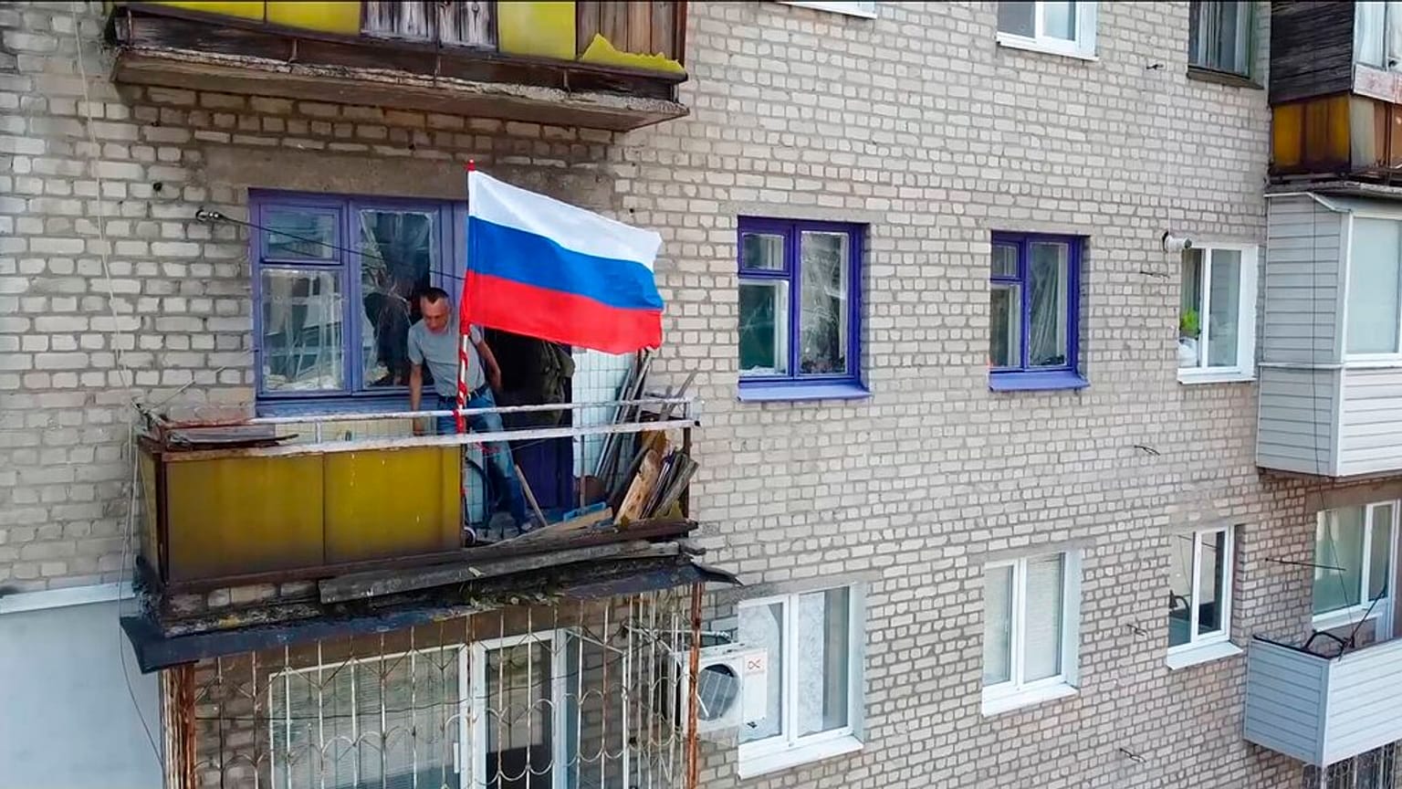 Ein Mann hisst eine Flagge auf einem Balkon in Lyssyschansk.
