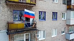 Ein Mann hisst eine Flagge auf einem Balkon in Lyssyschansk.