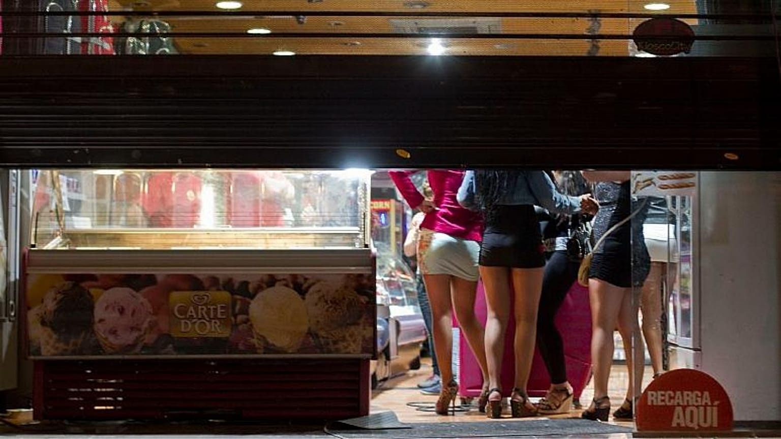 Prostitutes hide from riot police inside of a store during the eviction of a few activists who gathered at Puerta del Sol square in Madrid